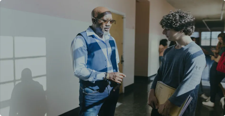 Mentor speaking with a student in a school hallway, providing guidance and support during a conversation