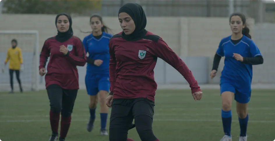 Young women competing in a soccer match, with a player in a maroon jersey controlling the ball while opponents pursue