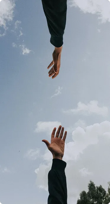 Two outstretched hands reaching toward each other against a cloudy blue sky, symbolizing connection, support, and teamwork