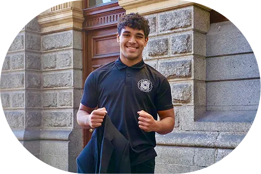 Young man wearing a black polo shirt standing outside a stone building